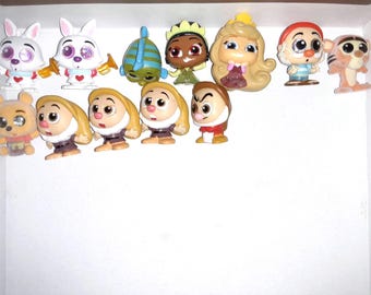 Puede incluir: Una colección de 12 pequeñas figuras de plástico de personajes de Disney. Los personajes incluyen Blancanieves, los enanos, Alicia en el País de las Maravillas y otros. Las figuras están todas en una caja blanca.