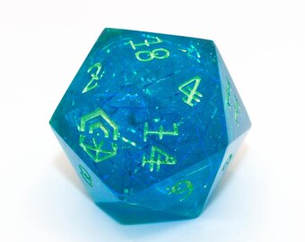 Könnte beinhalten: Ein blau-grüner, zwanzigseitiger Würfel. Der Würfel hat grüne Zahlen und Symbole in einem durchscheinenden blauen Körper. Er ist für Tabletop-Spiele konzipiert und vor einem weißen Hintergrund platziert.