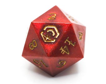 Könnte beinhalten: Ein roter, vielseitiger Würfel mit goldfarbenen Zahlen und Symbolen. Der Würfel hat eine glitzernde Textur und ist vor einem weißen Hintergrund platziert. Die Zahlen sind gut sichtbar, und der Würfel scheint aus Harz zu bestehen.