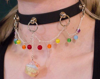 Könnte beinhalten: Schwarze Halskette mit silbernen Kettenakzenten und bunten Perlen. Ein großer, mehrfarbiger, durchscheinender, polyedrischer Würfel hängt in der Mitte. Die Halskette hat einen Regenbogen an Farben.