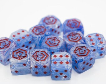 Könnte beinhalten: Eine Ansammlung von blau-weiß marmorierten Würfeln mit roten Symbolen und Augen. Die Würfel liegen auf einer weißen Oberfläche und zeigen ihr einzigartiges Design und ihre Farbvariationen. Geeignet für Tischspiele.