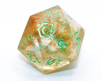 Könnte beinhalten: Ein klarer, vielseitiger D20-Würfel mit grünen Zahlen und Symbolen. Das Innere weist eine Mischung aus goldenem und grünem Glitzer auf, wodurch ein schimmernder Effekt entsteht. Der Würfel ist vor einem weißen Hintergrund platziert.