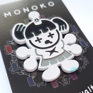 以下が含まれることがあります： 白のエナメルピンで、黒と白の漫画のキャラクターが描かれています。キャラクターは、頭蓋骨のような体と十字形の目をしています。背景には「MONOKO」という文字が見えます。