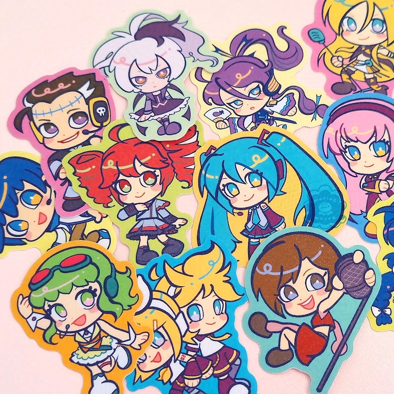 Photo of glittery stickers by marinewaltz. They are bright and colourful, and feature these synths: Hatsune Miku, Kagamine Rin and Len, Megurine Luka, SynthV Kasane Teto, Kamui Gakupo, GUMI, KAITO, MEIKO, VFlower, Big Al, Lily and Otomachi Una.