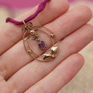 Op de afbeelding: Een delicate gouden ketting met een hanger van paarse amethist. De hanger heeft een cirkelvormig ontwerp met ingewikkelde details en een klein blaadjesmotief.