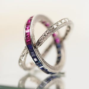 May include: A silver ring with three bands intertwined. The bands are set with blue sapphires, pink rubies, and diamonds.