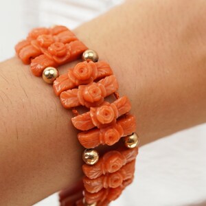 May include: A coral bracelet with gold beads and carved rose designs. The bracelet is made of orange coral and has a delicate, feminine look.