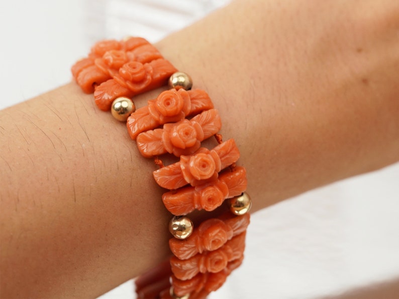 May include: A coral bracelet with gold beads and carved rose designs. The bracelet is made of orange coral and has a delicate, feminine look.