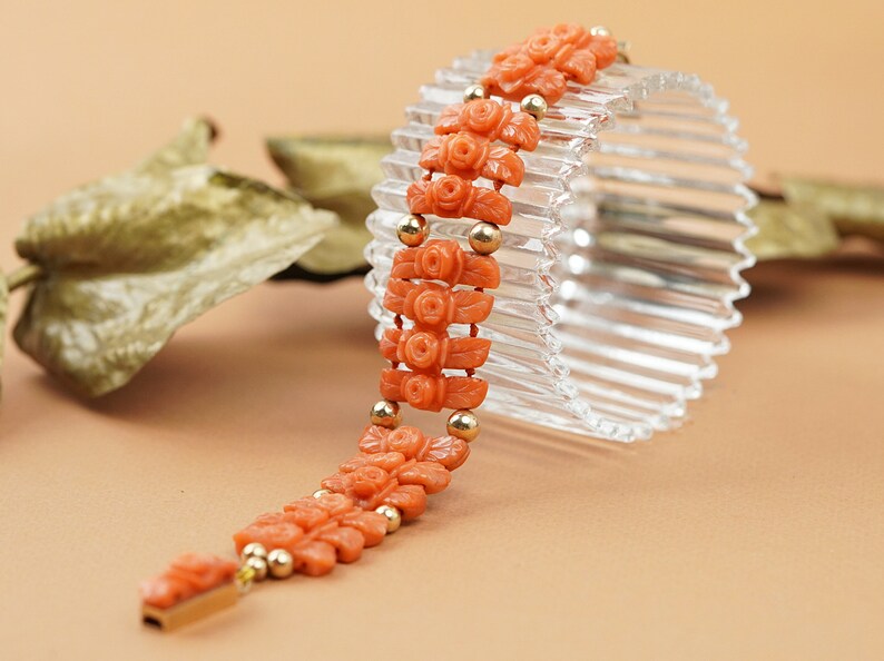 May include: A coral bracelet with carved rose motifs and gold beads. The bracelet is displayed on a clear glass stand.