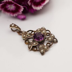 May include: A silver pendant with a purple gemstone surrounded by pearls. The pendant is in the shape of a flower with intricate details.