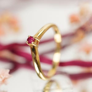 Può includere: Un delicato anello d'oro con una singola piccola pietra preziosa rossa rubino incastonata al centro.