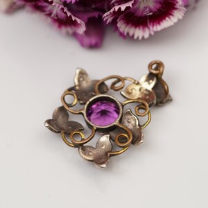 May include: A silver pendant with a purple gemstone set in a delicate, ornate design featuring butterfly motifs.