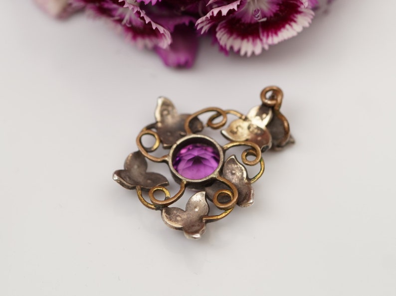 May include: A silver pendant with a purple gemstone set in a delicate, ornate design featuring butterfly motifs.