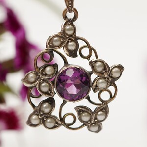 May include: A silver pendant with a purple gemstone surrounded by a delicate floral design and pearl accents.