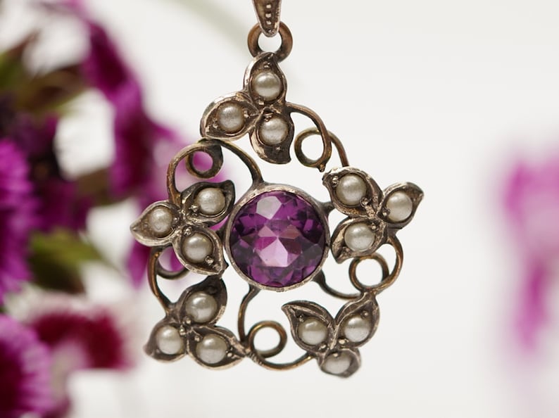 May include: A silver pendant with a purple gemstone surrounded by a delicate floral design and pearl accents.