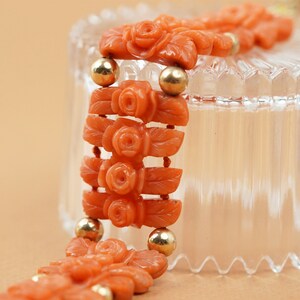 May include: A coral bracelet with carved rose motifs and gold beads. The bracelet is displayed on a clear glass surface.