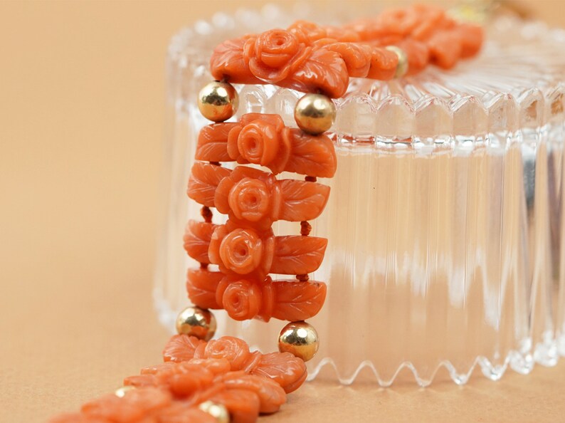 May include: A coral bracelet with carved rose motifs and gold beads. The bracelet is displayed on a clear glass surface.