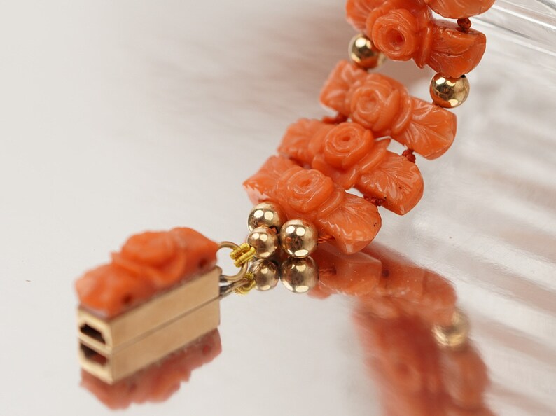 May include: A coral bracelet with gold beads and a rose design. The bracelet has a clasp made of gold.