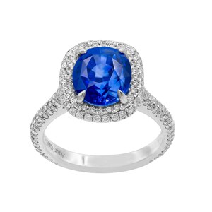 Puede incluir: Un anillo de platino con un gran zafiro ovalado rodeado de dos filas de diamantes. El anillo está grabado con "ART CARAT".