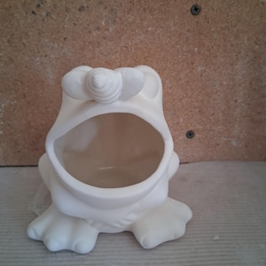 May include: A white ceramic frog-shaped container with an open mouth, designed to hold items. The frog has large eyes and webbed feet. The container is unpainted and ready for customization.