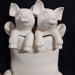 May include: A ceramic sculpture featuring two white pigs peering over the edge of a textured bag. The pigs have detailed facial features and are positioned side-by-side. The sculpture is unpainted and ready for customization.