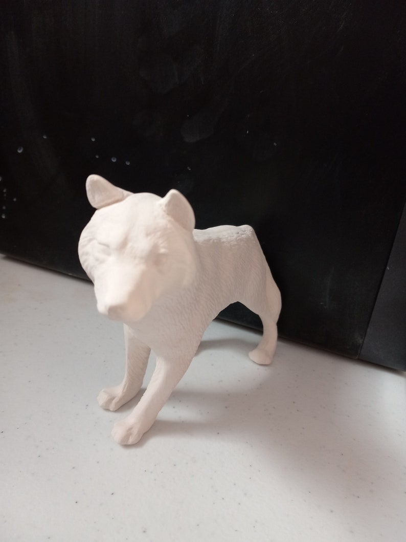 May include: White ceramic wolf figurine with a textured surface. The wolf is standing on all four legs with its head tilted slightly down.