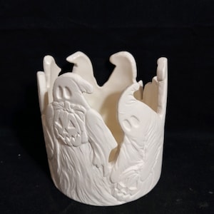 May include: White ceramic candle holder shaped like a ring with ghost and pumpkin faces carved into the sides.