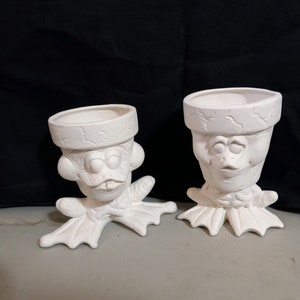 May include: Two white ceramic frog planter pots with whimsical faces. The frog planters have textured surfaces and are ready to be painted.
