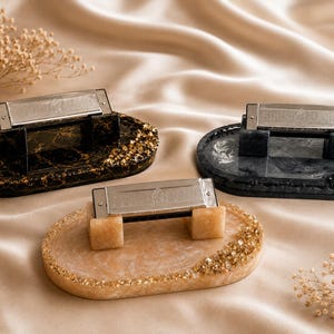 May include: Three oval resin trays, each featuring a metallic harmonica held by two matching resin blocks. One tray is black with gold flakes, one is dark gray with black accents, and one is a light beige marble pattern with gold leaf edges.