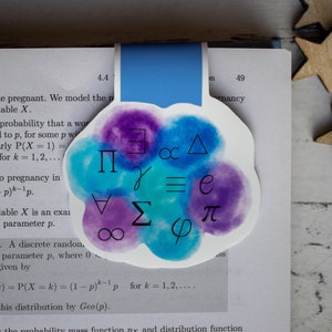May include: A watercolour bookmark with a blue and purple background featuring mathematical symbols including pi, sigma, infinity, delta, and epsilon. The bookmark is shaped like a cloud and has a blue ribbon.