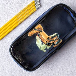 May include: A blue pencil case with a clear plastic front featuring a graphic of a robot arm. The case is closed and has a zipper.