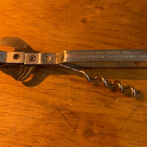 May include: A silver can opener and corkscrew combination tool. The tool is made by Henry Squire and Sons, Wholesale Cutlers, Chicago.