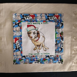 May include: A white pillowcase with a blue and white border featuring a dog wearing a Santa hat. The text on the pillowcase reads "He's making a list, I've eaten it twice."