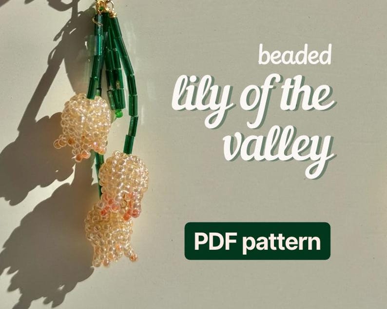 May include: A beaded lily of the valley design. The image shows two beaded lily of the valley flowers with green stems and a gold-colored clasp. The text on the image says "beaded lily of the valley" and "PDF pattern".