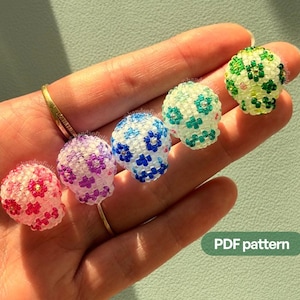 Puede incluir: Cinco pequeños adornos tridimensionales con forma de calavera hechos de diminutas cuentas de vidrio de colores. Cada calavera presenta un patrón floral distinto en rosa, morado, azul, turquesa o verde. El texto PDF pattern es visible.