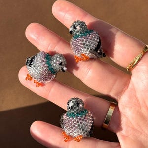 Puede incluir: Tres figuritas de palomas con cuentas. Las aves son principalmente plateadas con toques de color turquesa, morado y naranja. Las figuritas son peque&ntilde;as y detalladas, con peque&ntilde;as cuentas que forman el cuerpo y las alas.