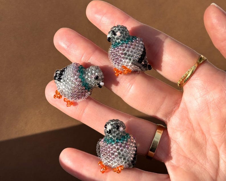 Puede incluir: Tres figuritas de palomas con cuentas. Las aves son principalmente plateadas con toques de color turquesa, morado y naranja. Las figuritas son peque&ntilde;as y detalladas, con peque&ntilde;as cuentas que forman el cuerpo y las alas.