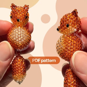 May include: A beaded fox figurine crafted from small orange, white, and black glass beads, featuring a round body, pointed ears, and a bushy tail. The text PDF pattern is visible in the center. The fox has black bead eyes and a black nose.