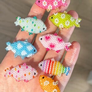 Puede incluir: Una colecci&oacute;n de peces de cuentas de colores, cada uno con un patr&oacute;n &uacute;nico. Los colores incluyen rosa, azul, verde y naranja. Peque&ntilde;os objetos decorativos, posiblemente para manualidades o joyer&iacute;a.