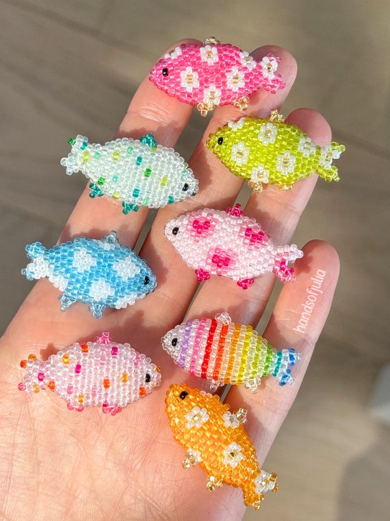 Puede incluir: Una colecci&oacute;n de peces de cuentas de colores, cada uno con un patr&oacute;n &uacute;nico. Los colores incluyen rosa, azul, verde y naranja. Peque&ntilde;os objetos decorativos, posiblemente para manualidades o joyer&iacute;a.