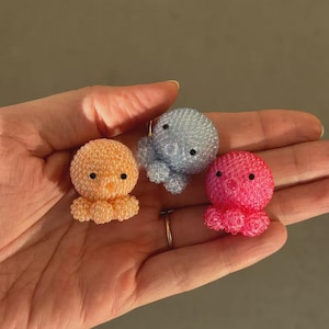 Puede incluir: Tres figuras de pulpos con cuentas en naranja, azul y rosa. Cada pulpo tiene ojos negros y un cuerpo redondeado y texturizado con tent&aacute;culos rizados. Las figuras son peque&ntilde;as y parecen hechas a mano.