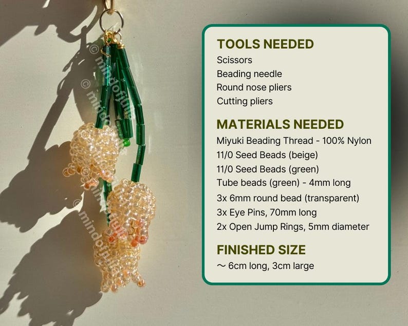 May include: A handmade beaded charm featuring two clusters of beige beads with green accents. The charm is suspended from a gold-colored ring. The image also includes a list of tools and materials needed to create the charm, and the finished size is approximately 6cm long and 3cm large.