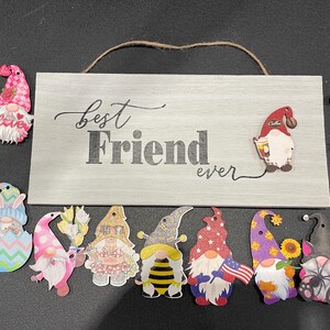 May include: A wooden sign with the words "Best Friend ever" and several gnome-shaped decorations. The gnomes are colorful and feature various designs, including flowers, coffee cups, and patriotic themes.