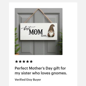 May include: A white wooden sign with the words "best MOM ever" in black script and block letters. A gnome with a brown and tan hat and white beard is on the right. The sign hangs from a natural rope.