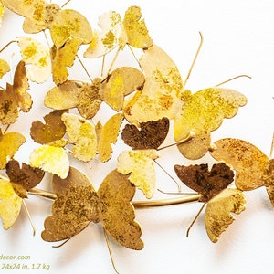 May include: Gold metal butterfly wall decor with 24x24 in. dimensions. The butterflies are arranged in a curved shape, resembling a branch. The butterflies have a textured, slightly distressed finish.