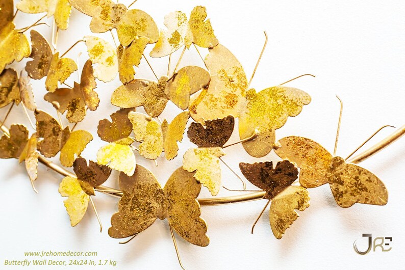 May include: Gold metal butterfly wall decor with 24x24 in. dimensions. The butterflies are arranged in a curved shape, resembling a branch. The butterflies have a textured, slightly distressed finish.