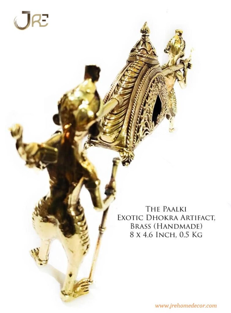May include: A gold-colored metal sculpture of a palanquin, a traditional Indian ceremonial litter, carried by two figures. The palanquin is decorated with intricate details and measures 8 inches by 4.6 inches. The sculpture is made of brass and weighs 0.5 kg. "THE PAALKI EXOTIC DHOKRA ARTIFACT, BRASS (HANDMADE) 8 X 4.6 INCH, 0.5 KG" is written below the sculpture.