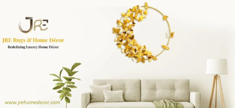 May include: Gold metal wall decor featuring a circle with a cluster of butterflies. The butterflies are arranged in a crescent shape on the left side of the circle. The decor is hanging on a white wall above a beige sofa.