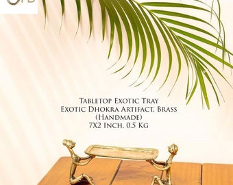 May include: A gold-colored metal tray with two figures holding it up. The tray is 7 inches by 2 inches and weighs 0.5 kg. The tray is handmade and is called a Dhokra artifact.  TABLETOP EXOTIC TRAY EXOTIC DHOKRA ARTIFACT, BRASS (HANDMADE) 7X2 INCH, 0.5 KG www.jrehomedecor.com