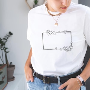 May include: White t-shirt with a black outline of a rectangle with flowers around it.